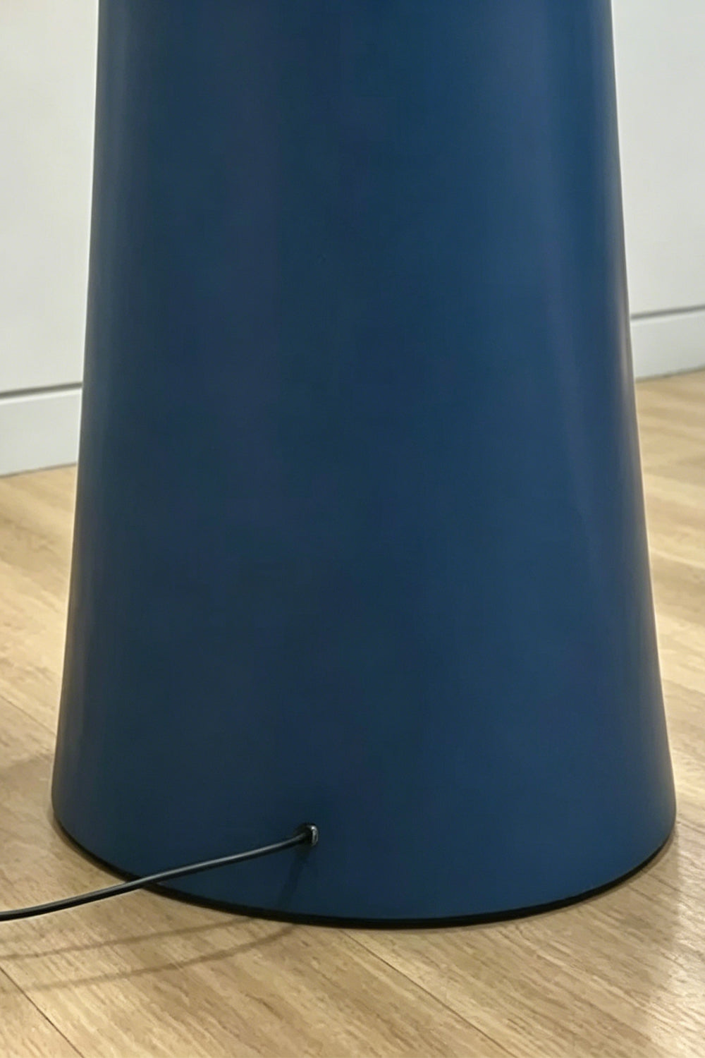 A tight close-up showing the sturdy base and cord connection point of the blue Cactus Luma Totem Floor Lamp on a light wood floor.