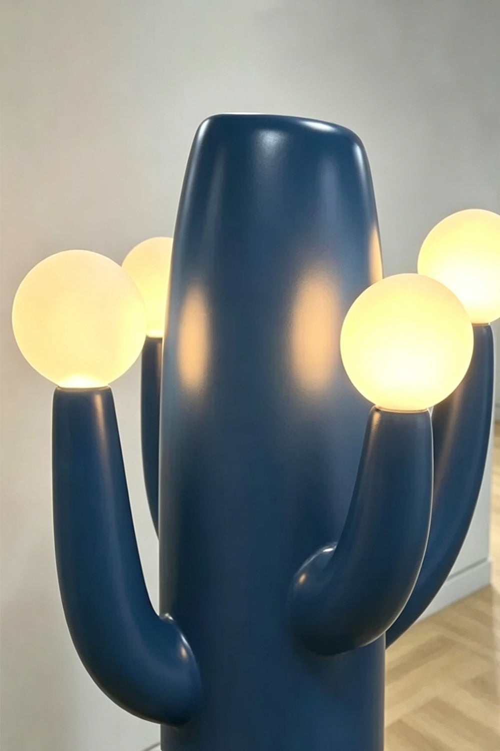 A detailed close-up shot of one illuminated spherical glass light bulb on a blue cactus arm of the totem floor lamp, showing the FRP material.