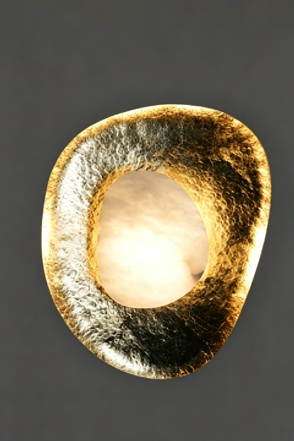 Caeliform Aurelia Alabaster Wall Lamp | Alabaster, Brass | Extensive close-up of the unlit lamp against a textured grey background, detailing the hand-hammered brass pattern | Isolated product shot | Samu Lamp