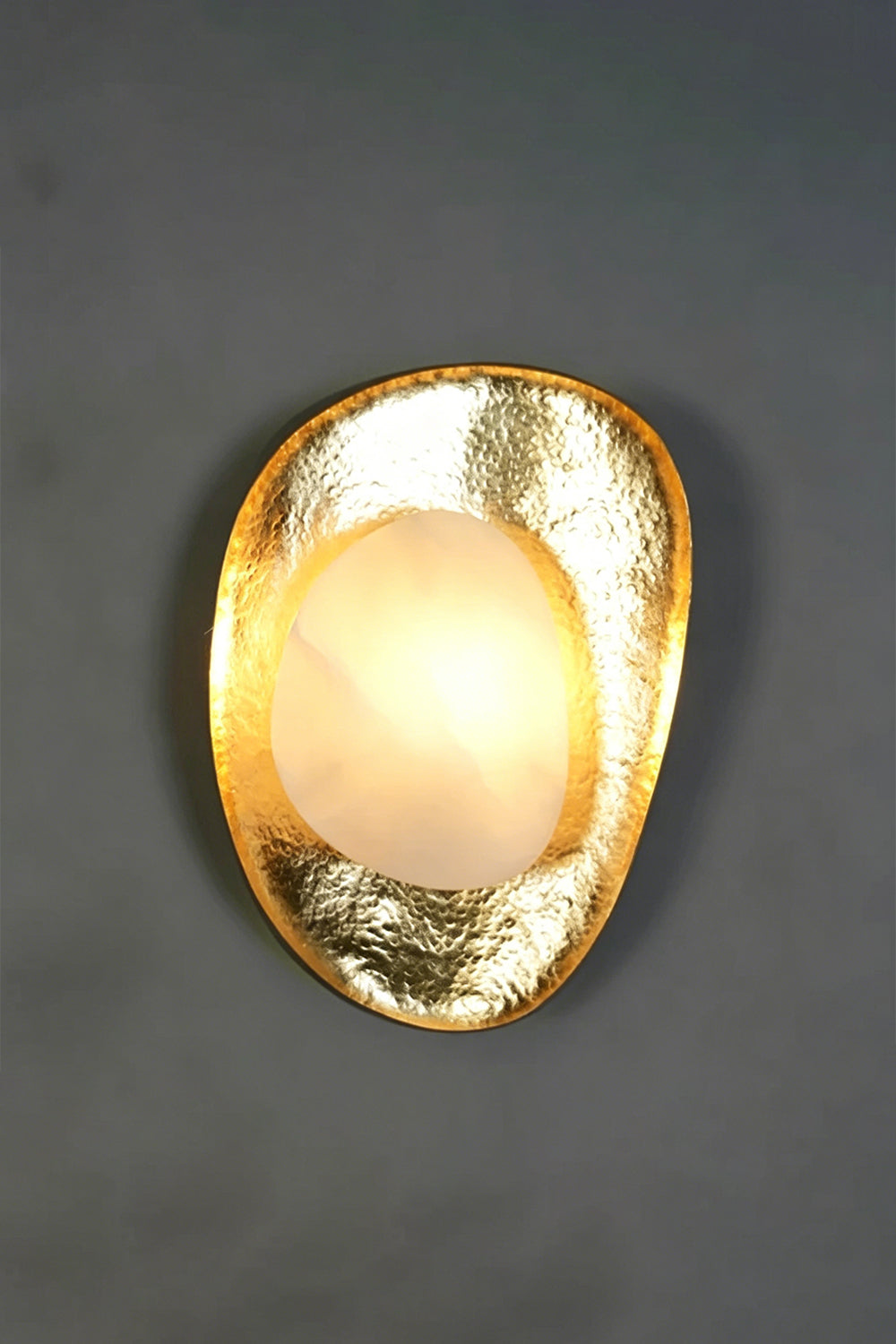 Caeliform Aurelia Alabaster Wall Lamp | Alabaster, Brass | Centrally positioned and fully lit against a dark textured wall, maximizing the warm glow effect | Samu Lamp