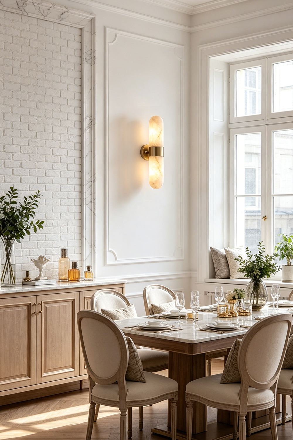Calla Alabaster Capsule Wall Sconce | Alabaster, Brass | Installed in a refined classical dining room casting a soft light near a wooden dining table and upholstered chairs | Samu Lamp