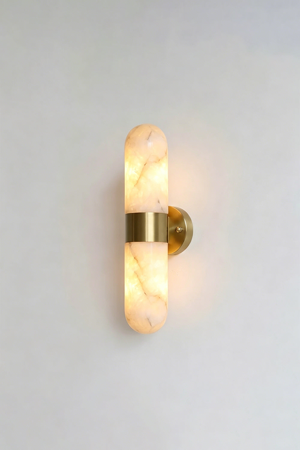 Calla Alabaster Capsule Wall Sconce | Alabaster, Brass | Alternative lit studio view of the brushed brass stone sconce radiating a soft warm white glow | Samu Lamp