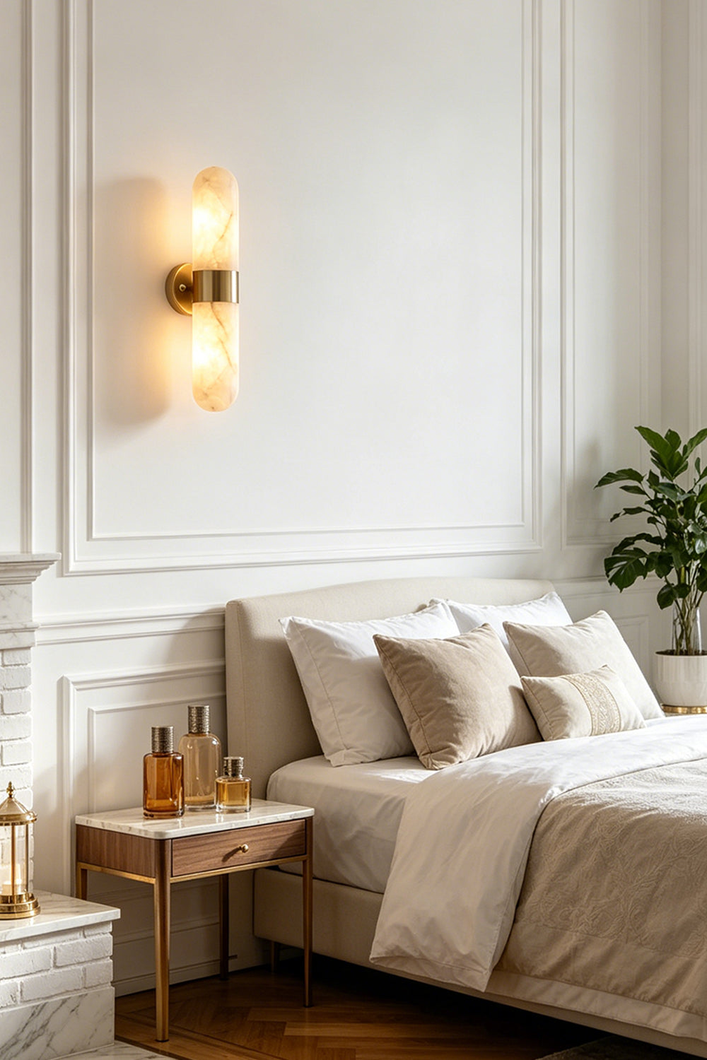 Calla Alabaster Capsule Wall Sconce | Alabaster, Brass | Serving as a cozy bedside reading lamp on a white wall beside a classic platform bed and a wooden nightstand | Samu Lamp