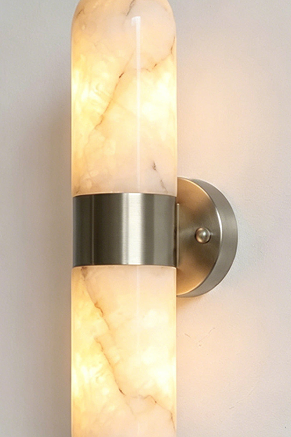 Calla Alabaster Capsule Wall Sconce | Alabaster, Metal | Close-up studio shot of the illuminated capsule wall fixture featuring the silver chrome hardware variant finish | Detail shot | Samu Lamp