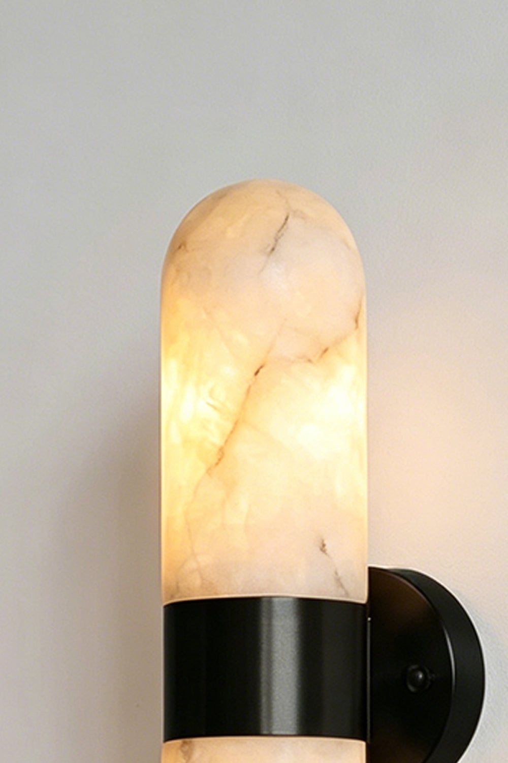 Calla Alabaster Capsule Wall Sconce | Alabaster, Metal | Close-up focus on the rounded dome of the glowing natural stone shade secured by a sleek matte black metal band | Detail shot | Samu Lamp