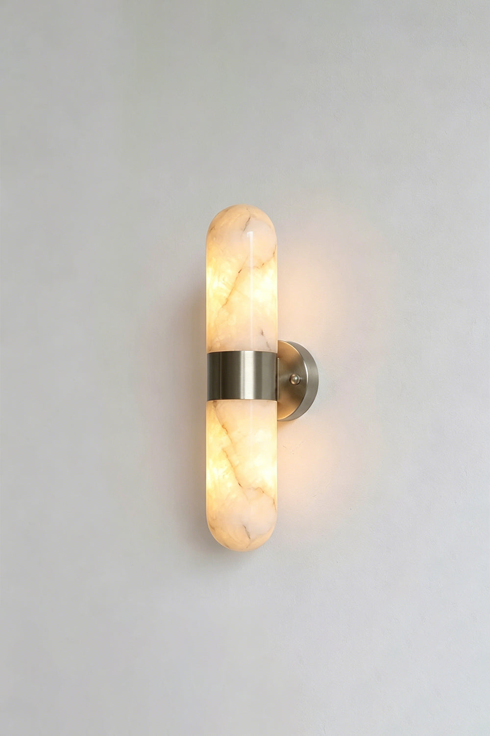 Calla Alabaster Capsule Wall Sconce | Alabaster, Metal | Another lit studio view of the polished chrome or silver nickel variant casting an elegant glow | Samu Lamp