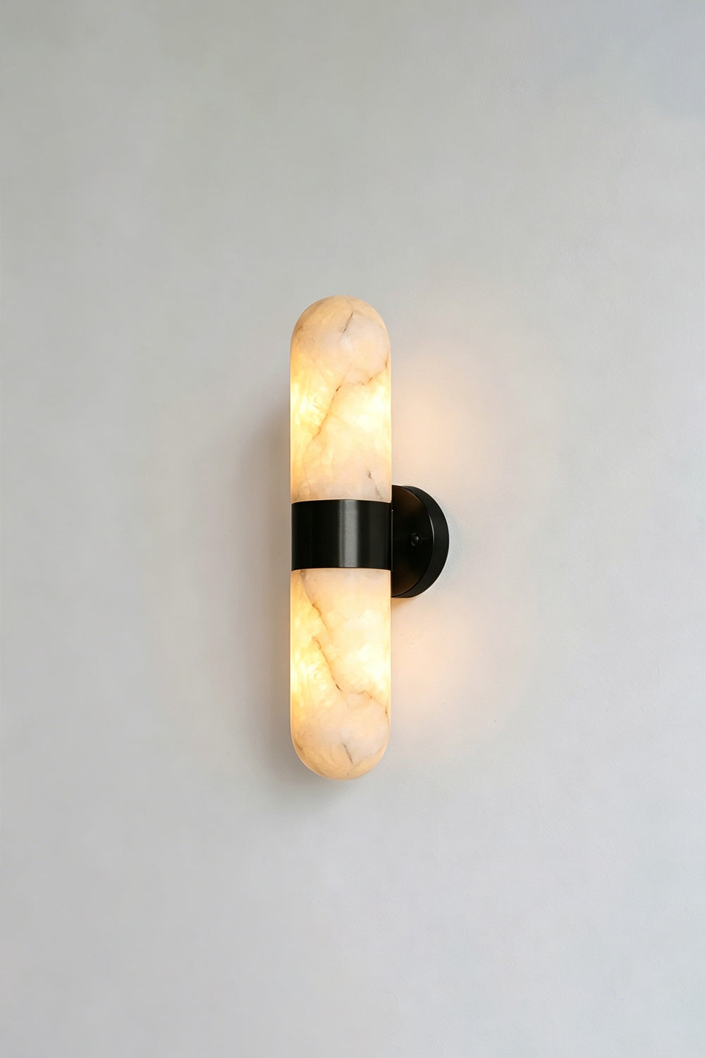 Calla Alabaster Capsule Wall Sconce | Alabaster, Metal | Lit studio view of the industrial modern matte black hardware finish variant against a white studio background | Samu Lamp