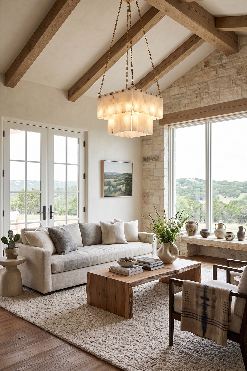 Callista Tiered Alabaster Chandelier | Alabaster, Metal | Hanging as a grand centerpiece in a rustic modern living room with high vaulted ceilings, exposed wooden beams, and a cream fabric sofa | Samu Lamp
