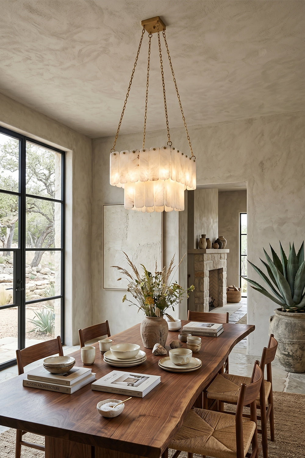 Callista Tiered Alabaster Chandelier | Alabaster, Metal | Suspended over a modern wooden dining table set with white tableware in a sophisticated dining room next to a large potted plant | Samu Lamp