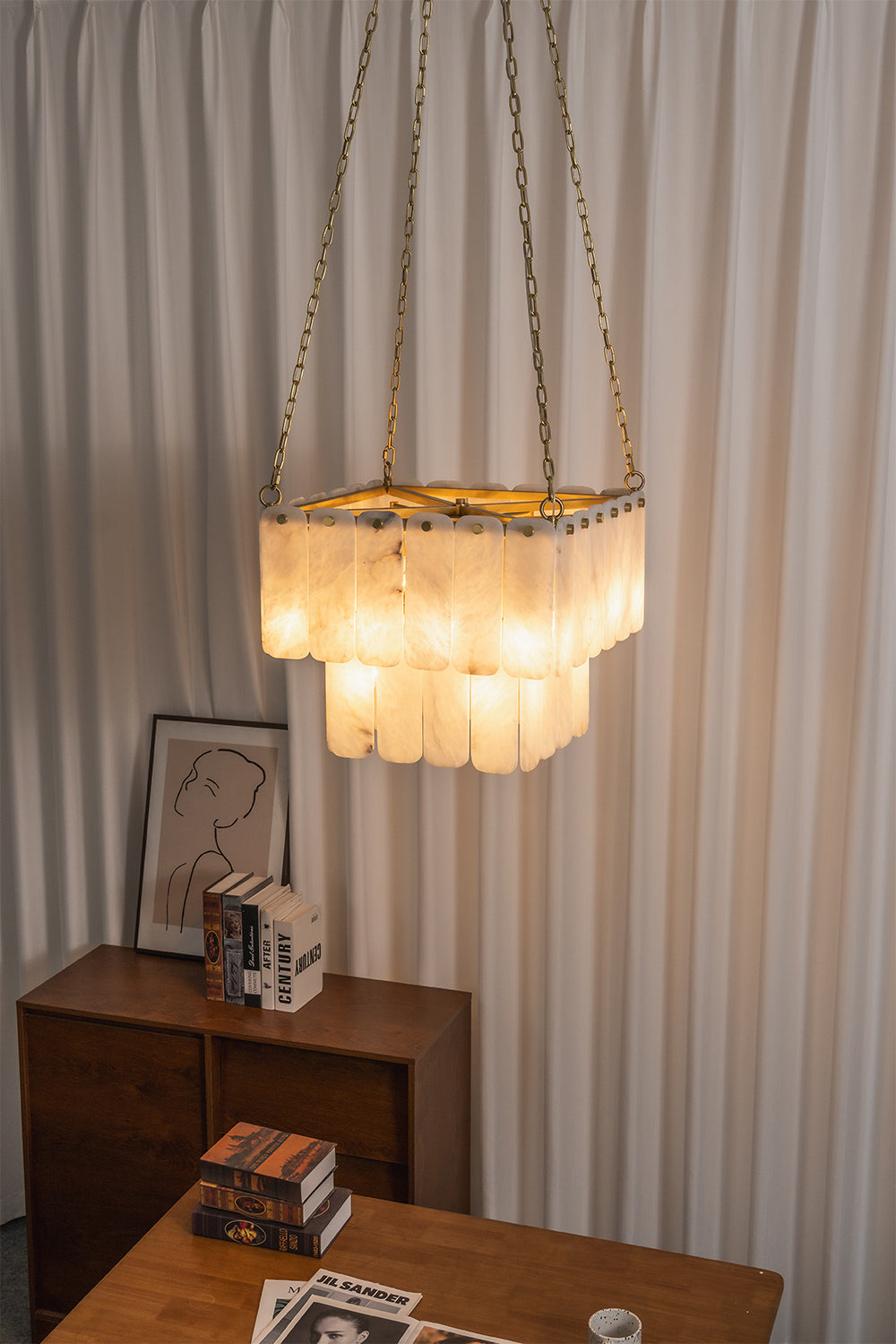Callista Tiered Alabaster Chandelier | Alabaster, Metal | Staged in a contemporary interior corner, casting a cozy golden ambient glow near vertically pleated curtains and a wooden chest | Samu Lamp