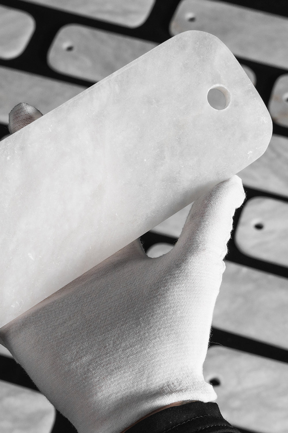Callista Tiered Alabaster Chandelier | Alabaster, Metal | A gloved hand holding up a single polished rectangular white alabaster stone component to demonstrate its opacity and fine texture | Detail shot | Samu Lamp