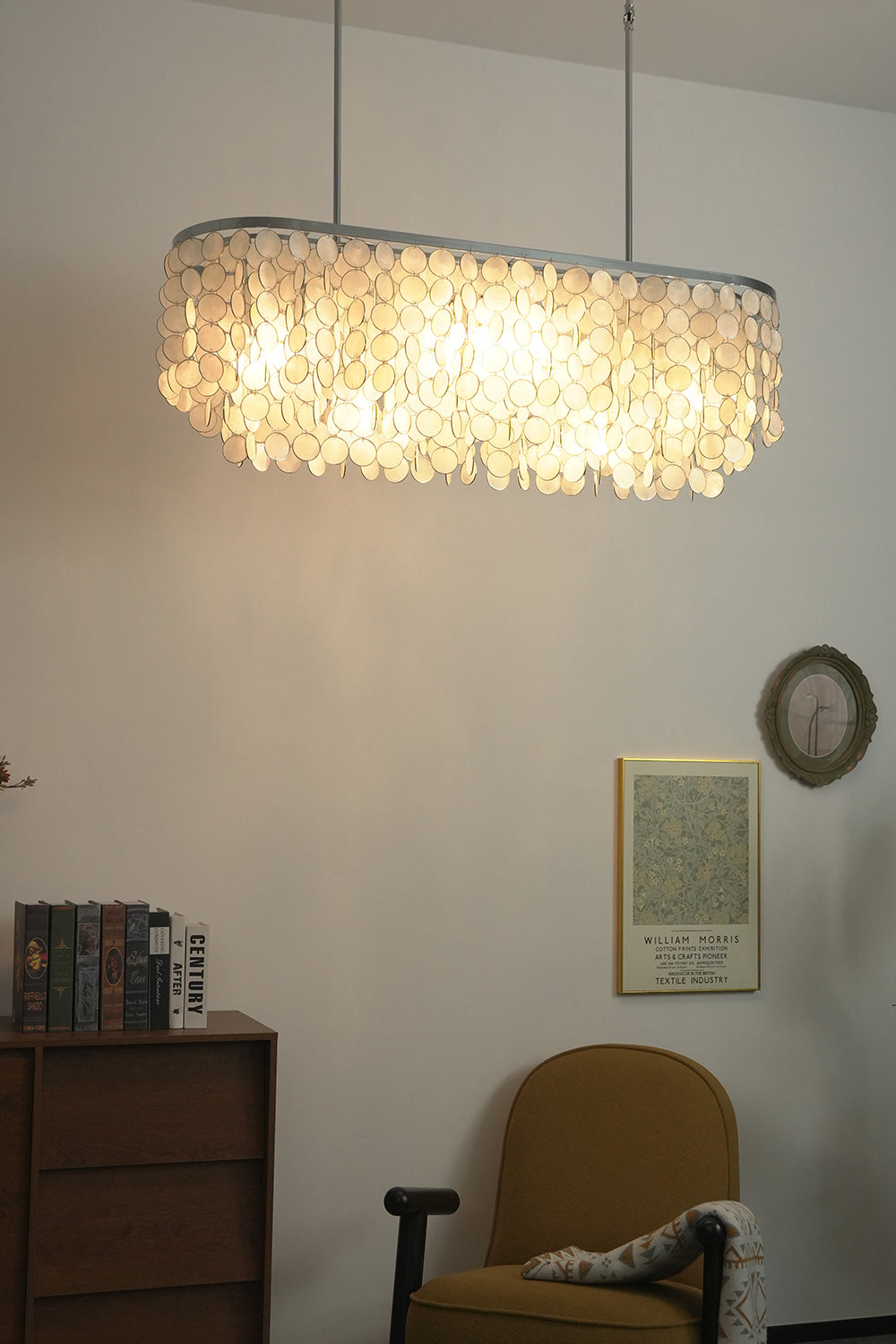 Elongated shell chandelier for workspace | Iron | Shell | Hanging in a modern corner with artwork and a yellow chair | Samu Lamp