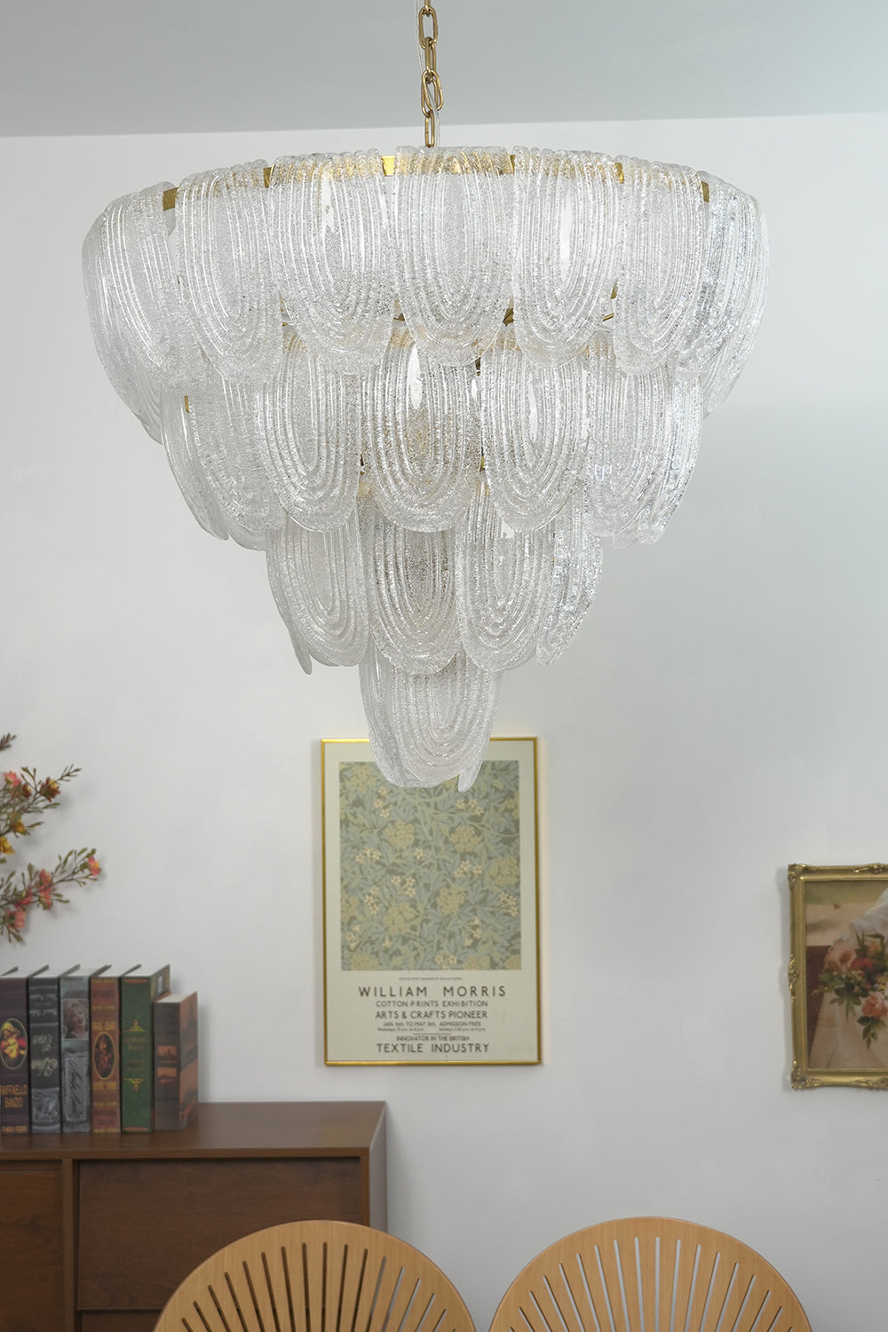 Lit tiered glass petal chandelier against white wall | Metal, Glass | Centered view showing the warm glowing texture | Samu Lamp