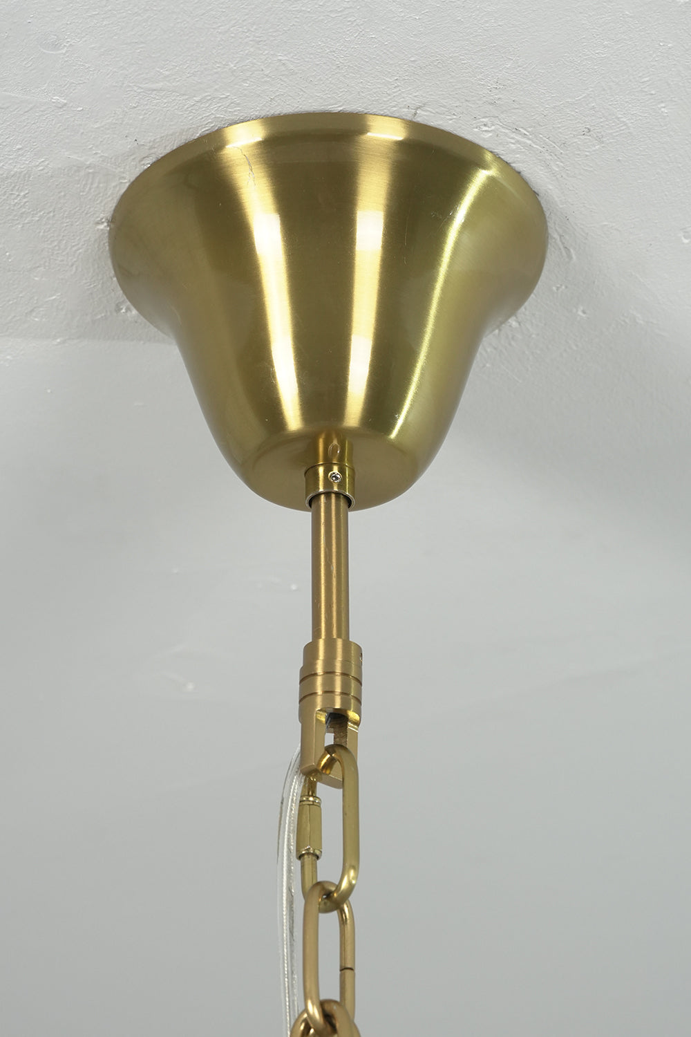 Brass ceiling canopy and chain connection detail | Metal | Close-up of the gold-finish mounting hardware | Samu Lamp