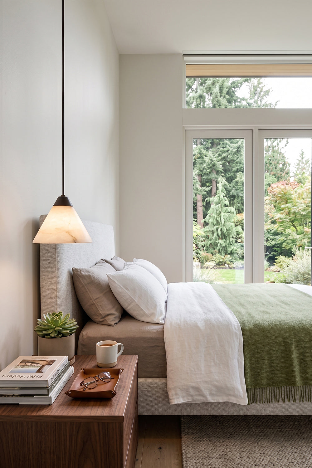 Caspian Conical Alabaster Pendant Light | Natural Alabaster and Brass | Suspended above a wooden nightstand in a cozy bedroom with neat green and white linens | Samu Lamp