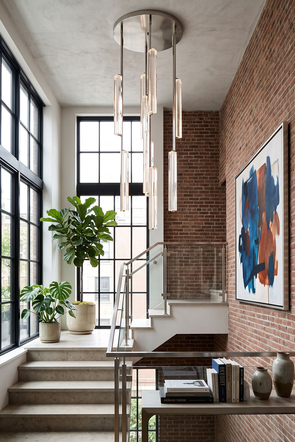 Cassian Cascading Crystal Ring Chandelier illuminating a modern stairway with brick walls and large windows.