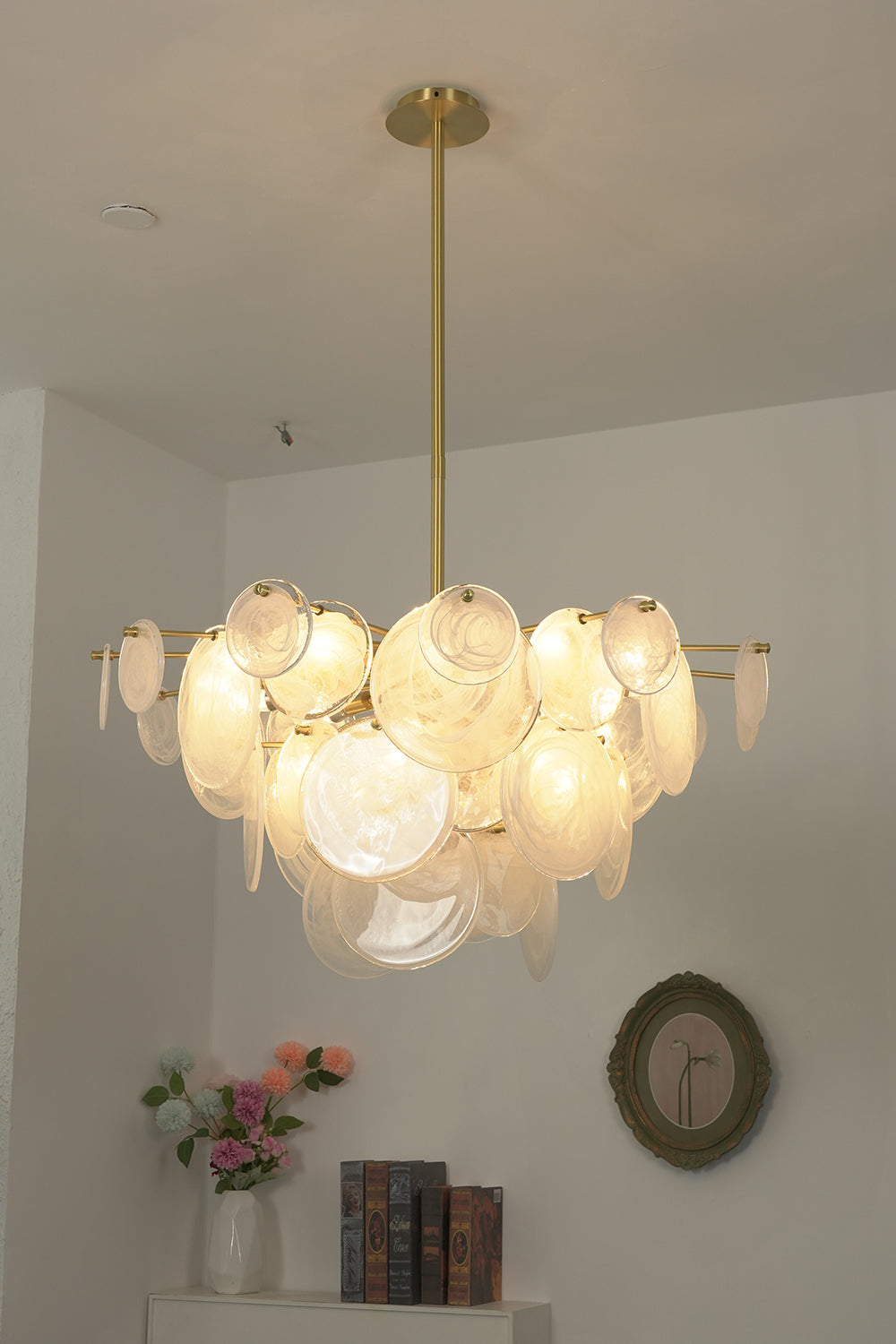 English: Celeste Glass Disc Chandelier | Glass, Metal | Studio view of the fully illuminated glass disc fixture casting a warm golden glow against a plain white wall | Samu Lamp
