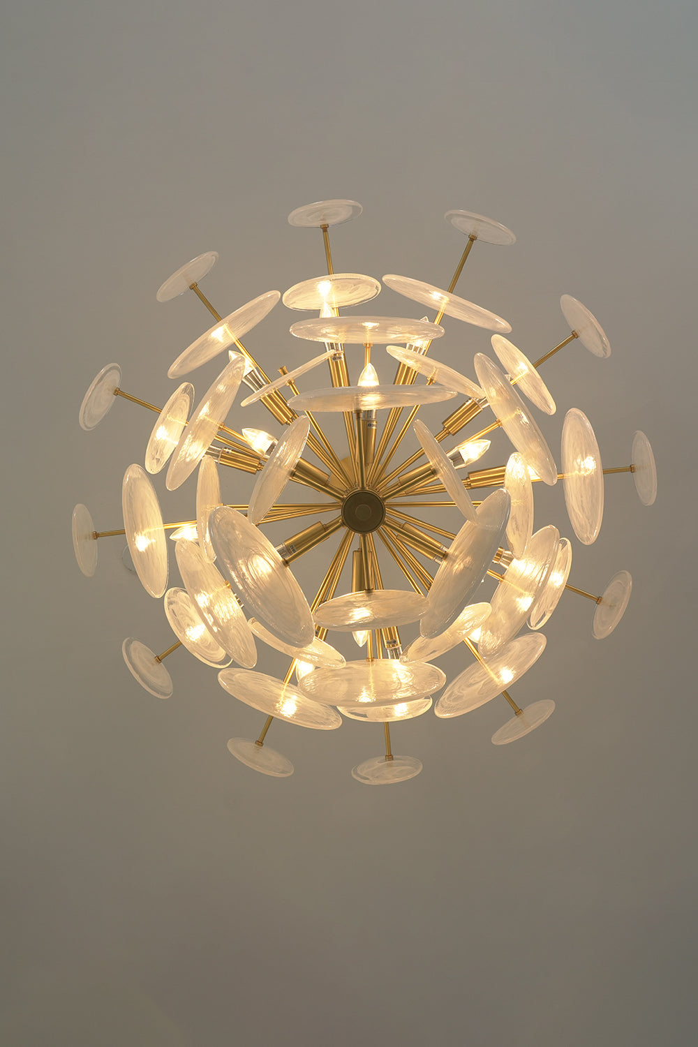 English: Celeste Glass Disc Chandelier | Glass, Metal | Direct bottom-up perspective looking into the glowing radial cluster of glass discs and gold brass frame spokes | Detail shot | Samu Lamp