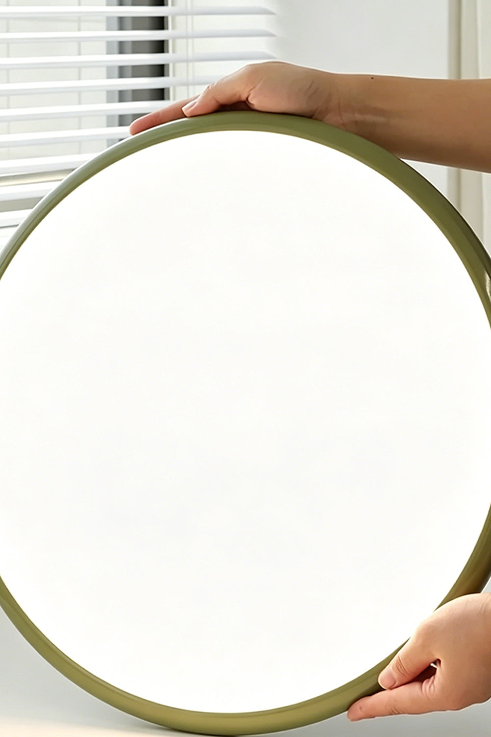 Celestial Disc Lacquered Ceiling Light | Acrylic, Metal | A person's hands holding the unlit green-trimmed circular light, demonstrating its large scale against a grey wall | Scale reference shot | Samu LampCelestial Disc