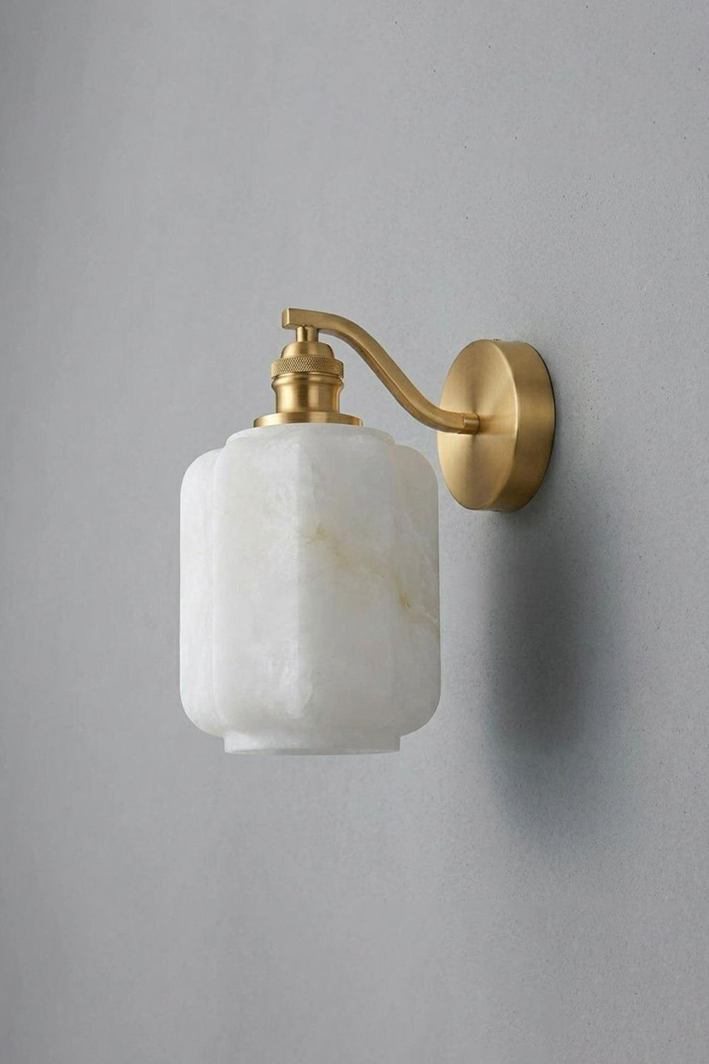 Cordelia Scalloped Alabaster Wall Sconce mounted on a gray wall with brass arm and alabaster shade.