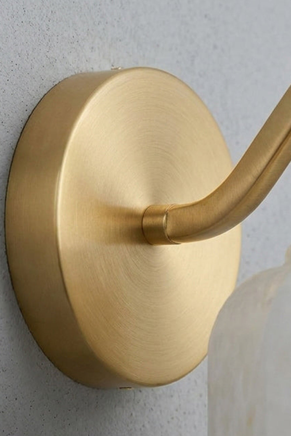 Cordelia Scalloped Alabaster Wall Sconce | Natural Alabaster and Brushed Brass | Detailed macro shot focusing on the smooth circular metal backplate and curved arm connection | Samu Lamp