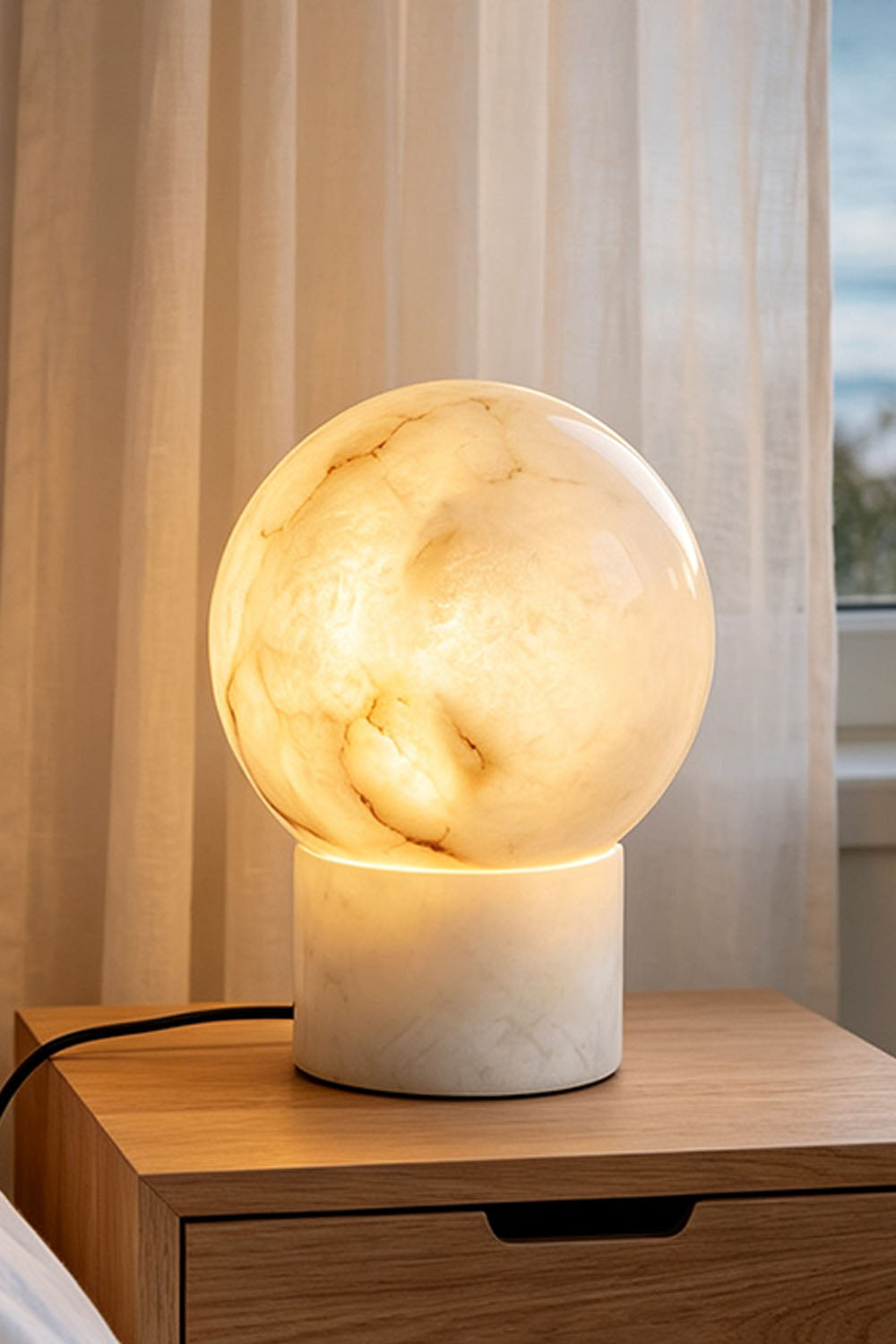 Cosima Alabaster Globe Table Lamp | Natural Alabaster | Standing on a wooden nightstand next to a white sheer curtain | Samu Lamp
