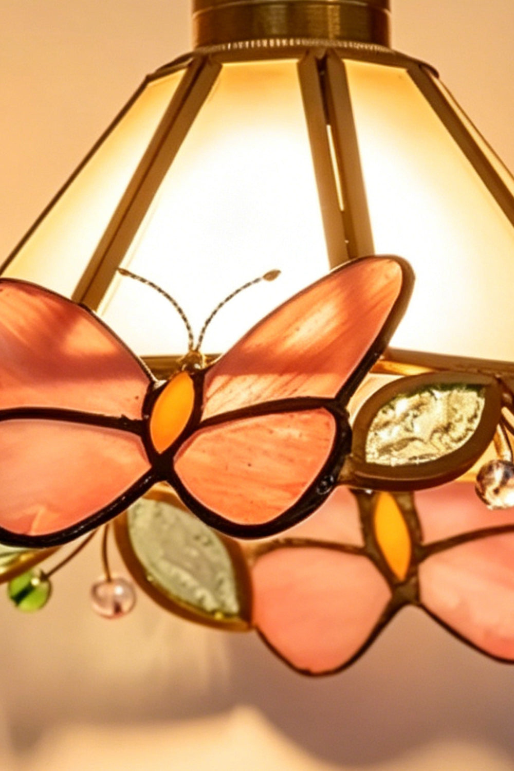 Cynthia Butterfly Articulated Wall Lamp | Stained Glass, Metal, Wood | Close-up view of the fully illuminated stained glass lampshade highlighting the vibrant pink and orange butterflies under warm light | Detail shot | Samu Lamp