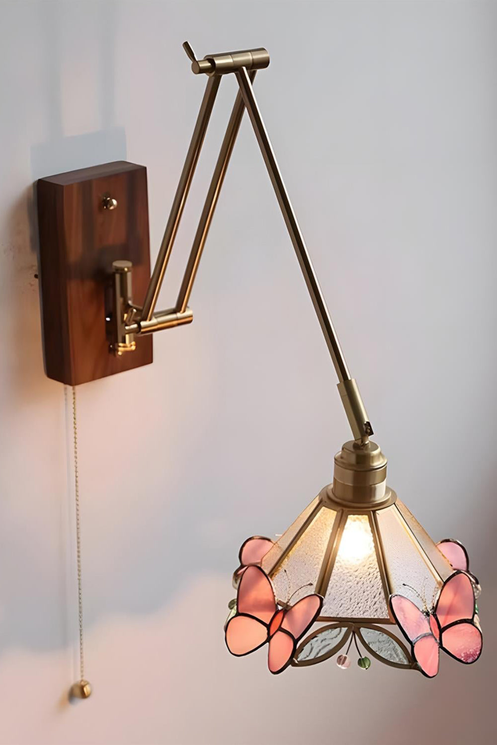 Cynthia Butterfly Articulated Wall Lamp | Stained Glass, Metal, Wood | Frontal angled view of the fully illuminated glass butterfly wall lamp casting a soft golden glow against a plain white wall | Samu Lamp