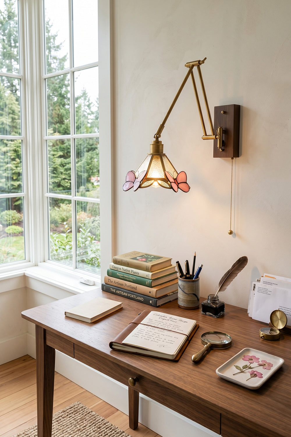 Cynthia Butterfly Articulated Wall Lamp | Stained Glass, Metal, Wood | Positioned as a functional desk task light over a traditional wooden writing table next to a large window with scenic views | Samu Lamp