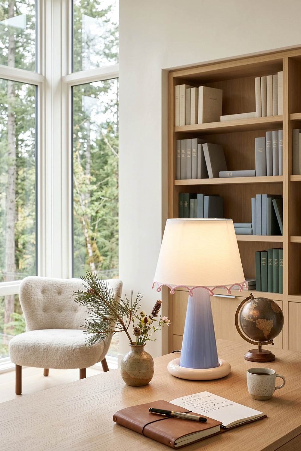 Dolce Ribbon Ceramic Table Lamp | Ceramic, Fabric | Tall shade variant providing a warm glow on a wooden desk with books and a globe in a cozy home library with large windows | Samu Lamp