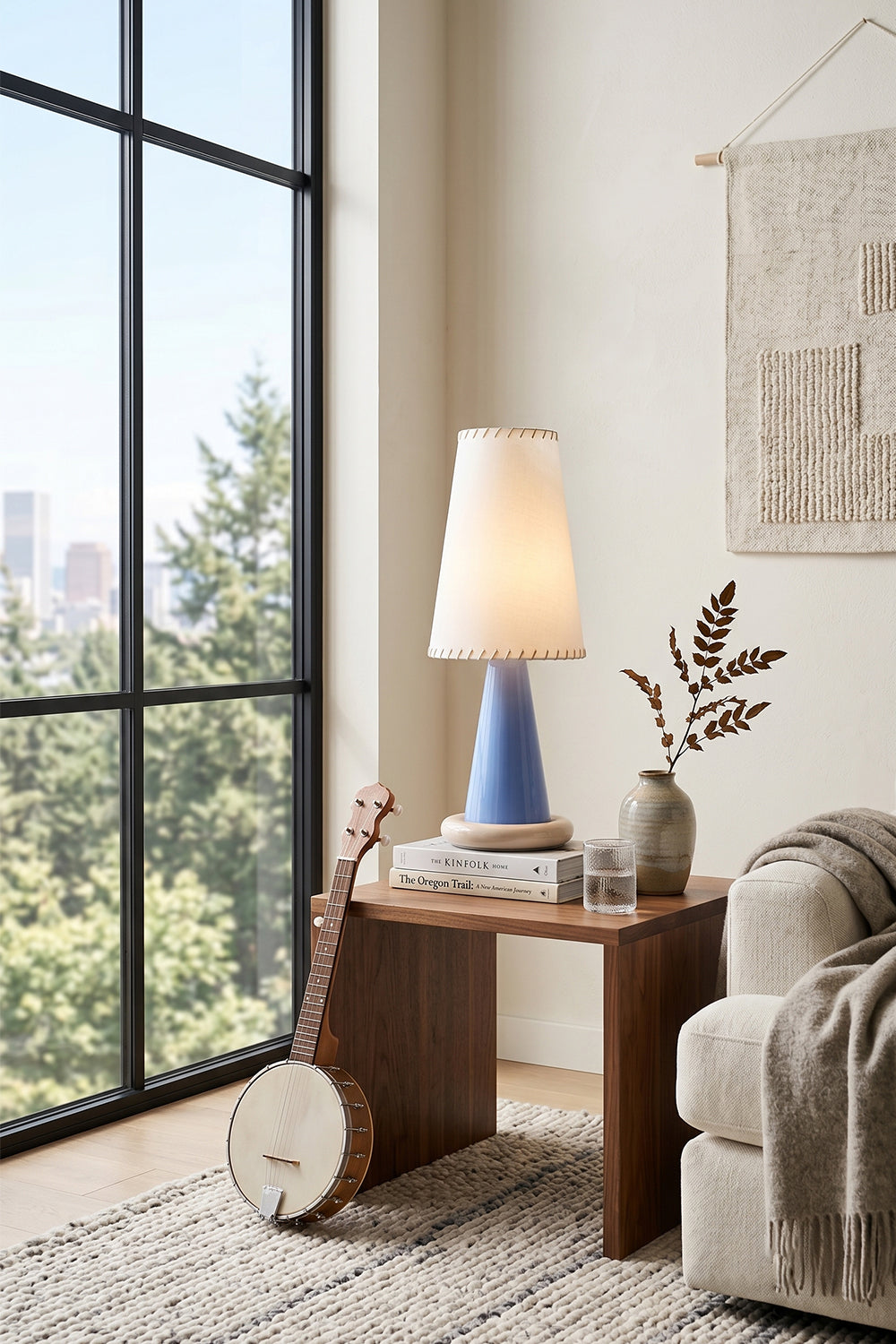 Dolce Ribbon Ceramic Table Lamp | Ceramic, Fabric | Styled on a dark wood end table next to a cozy beige sofa and a string instrument in a sunlit modern room nook | Samu Lamp
