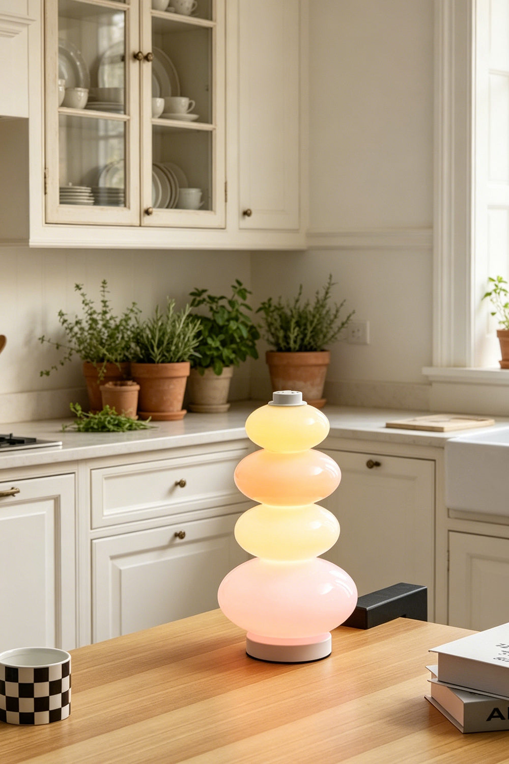 Dolce Stacked Pastel Glass Table Lamp | Glass, Metal | Standing as a playful accent on a warm wooden kitchen island table surrounded by potted green plants | Samu Lamp