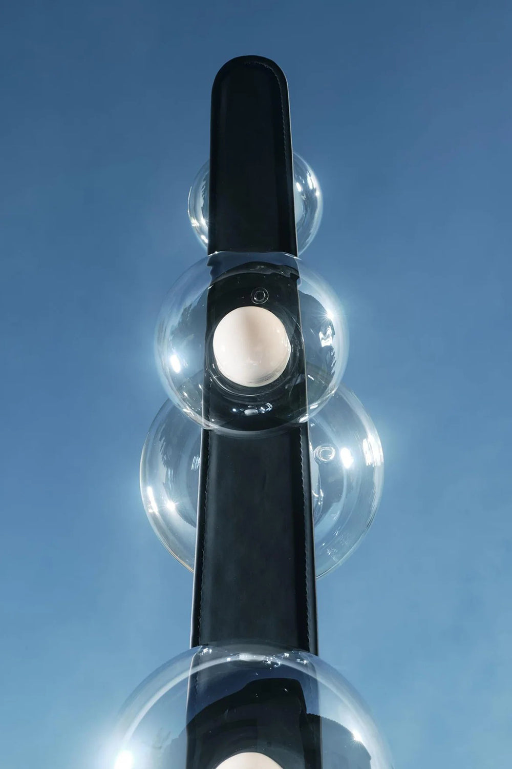 Drosia Dewdrop Floor Lamp | Glass, Metal | Low angle artistic shot looking up at the clear glass spheres on the black metallic pole against a bright blue sky background | Detail shot | Samu Lamp