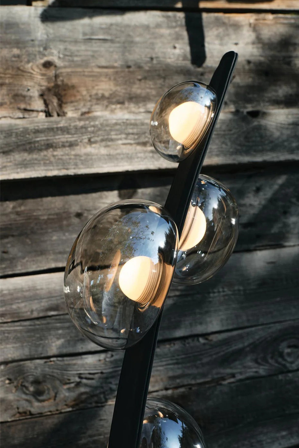 Drosia Dewdrop Floor Lamp | Glass, Metal | Close-up focus on the fully illuminated warm globe bulbs refracting light through the clear dewdrop glass shades against a rustic dark wooden wall | Detail shot | Samu Lamp