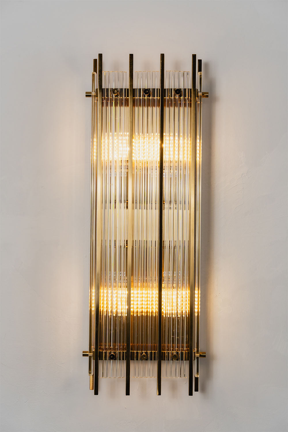 Drystan Ribbed Glass Brass Wall Lamp illuminated on a wall showcasing its elegant design.