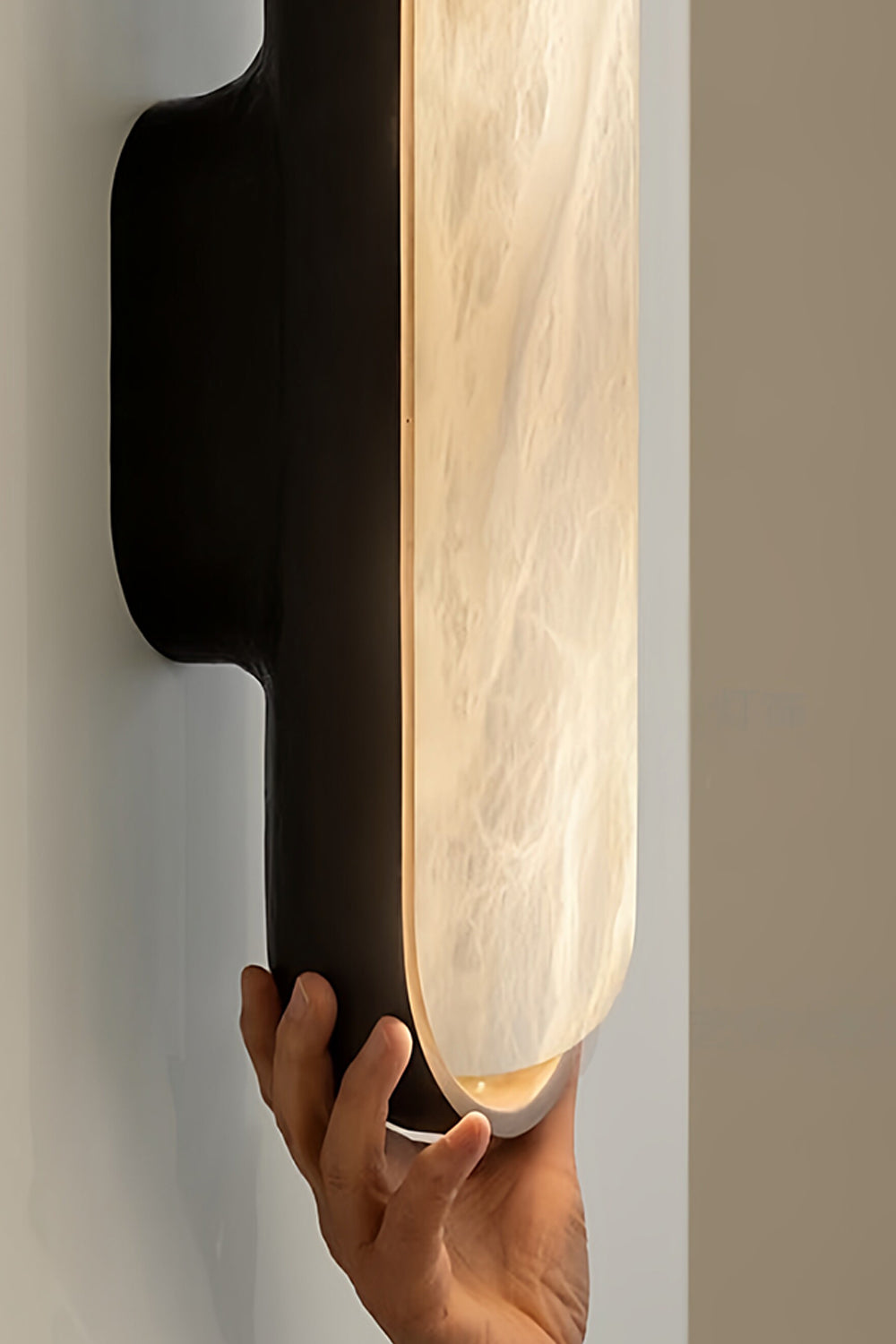 Elara Capsule Alabaster Wall Sconce with hand showcasing the alabaster diffuser and matte black casing.