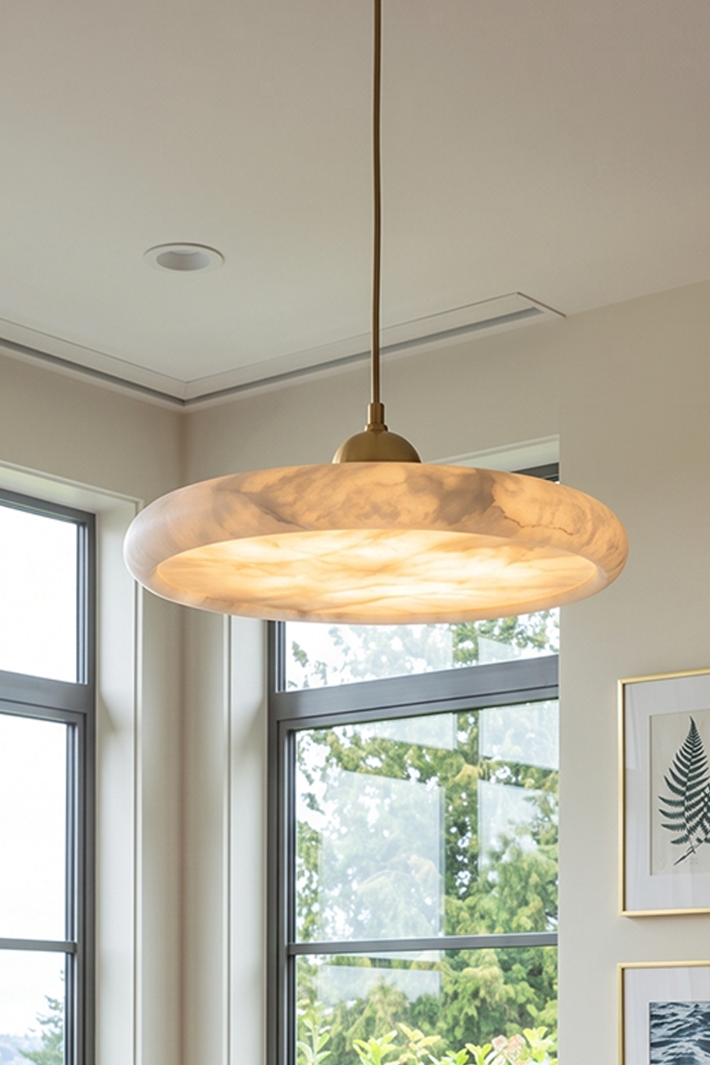 Elowen Alabaster Disc Pendant Light | Natural Alabaster and Brass | Displayed hanging near a bright window wall casting a soft inviting light into the interior space | Samu Lamp