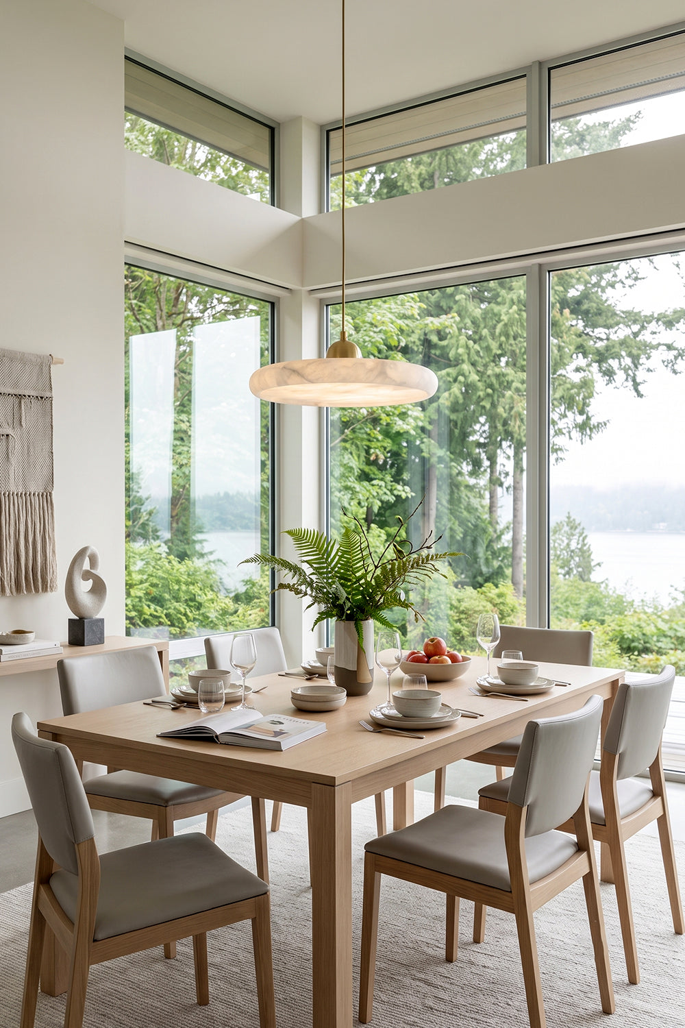 Elowen Alabaster Disc Pendant Light | Natural Alabaster and Brass | Hanging above a modern wooden dining table in a bright room with panoramic forest window views | Samu Lamp