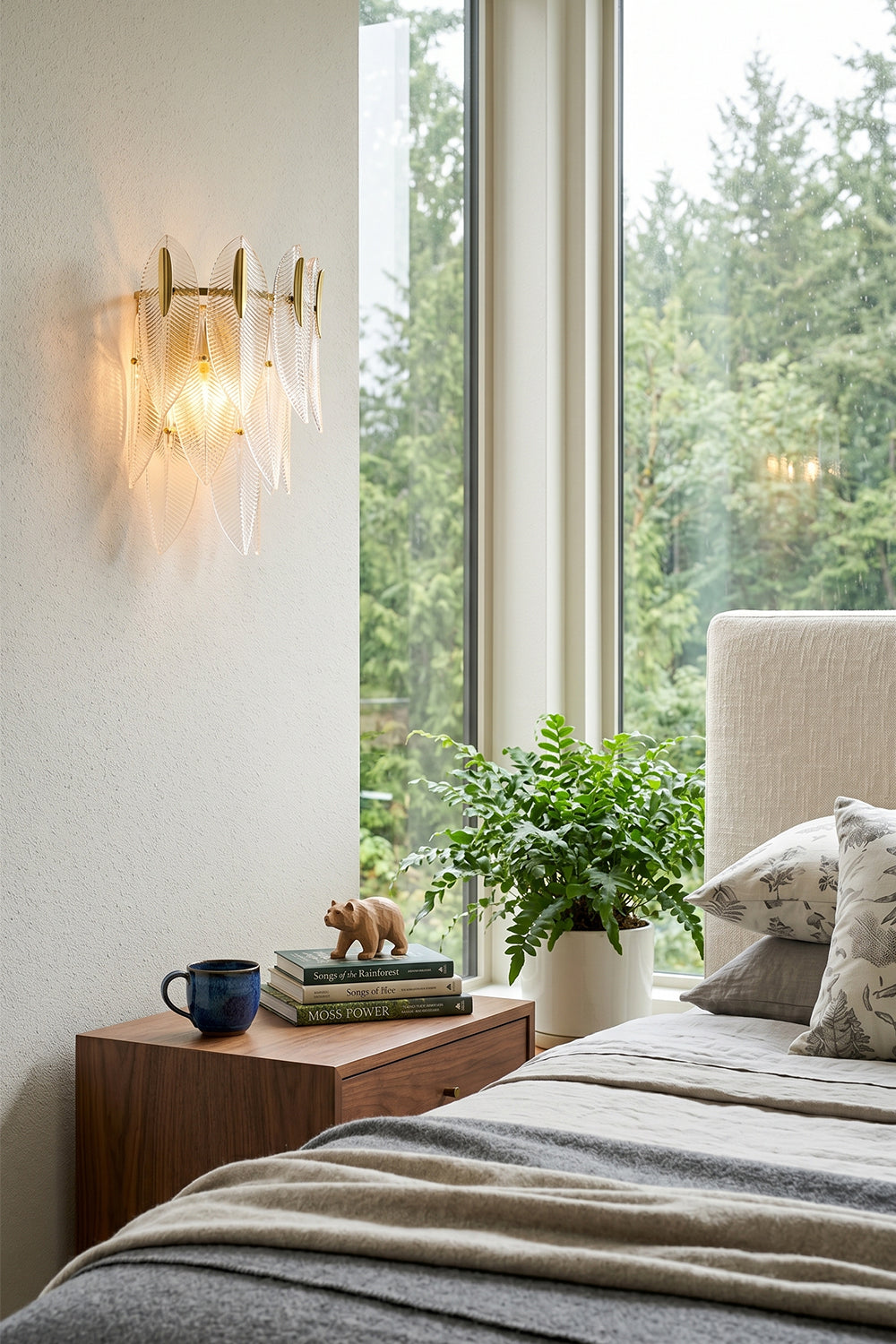 Elowen Cascading Glass Wall Lamp | Glass, Metal | Mounted as a cozy bedtime reading light on a white wall next to a plush bed and a sunlit window with a forest view | Samu Lamp