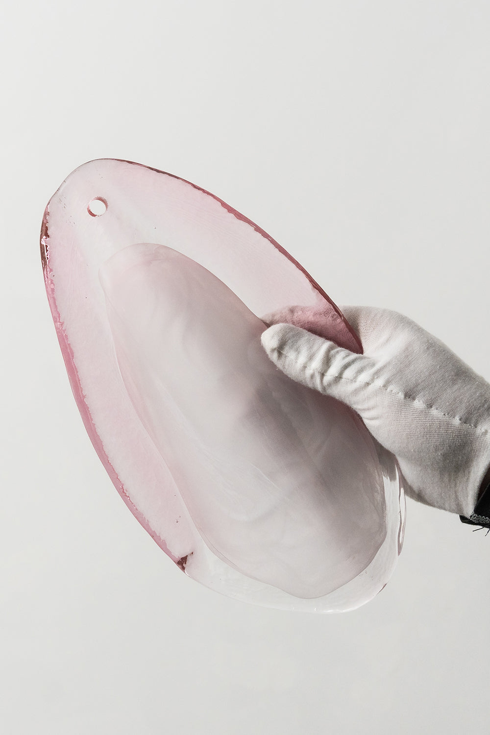 Elysian Bloom Glass Wall Lamp | Metal, Glass | A gloved hand holding a single translucent pink glass petal to show size and texture | Detail shot | Samu Lamp