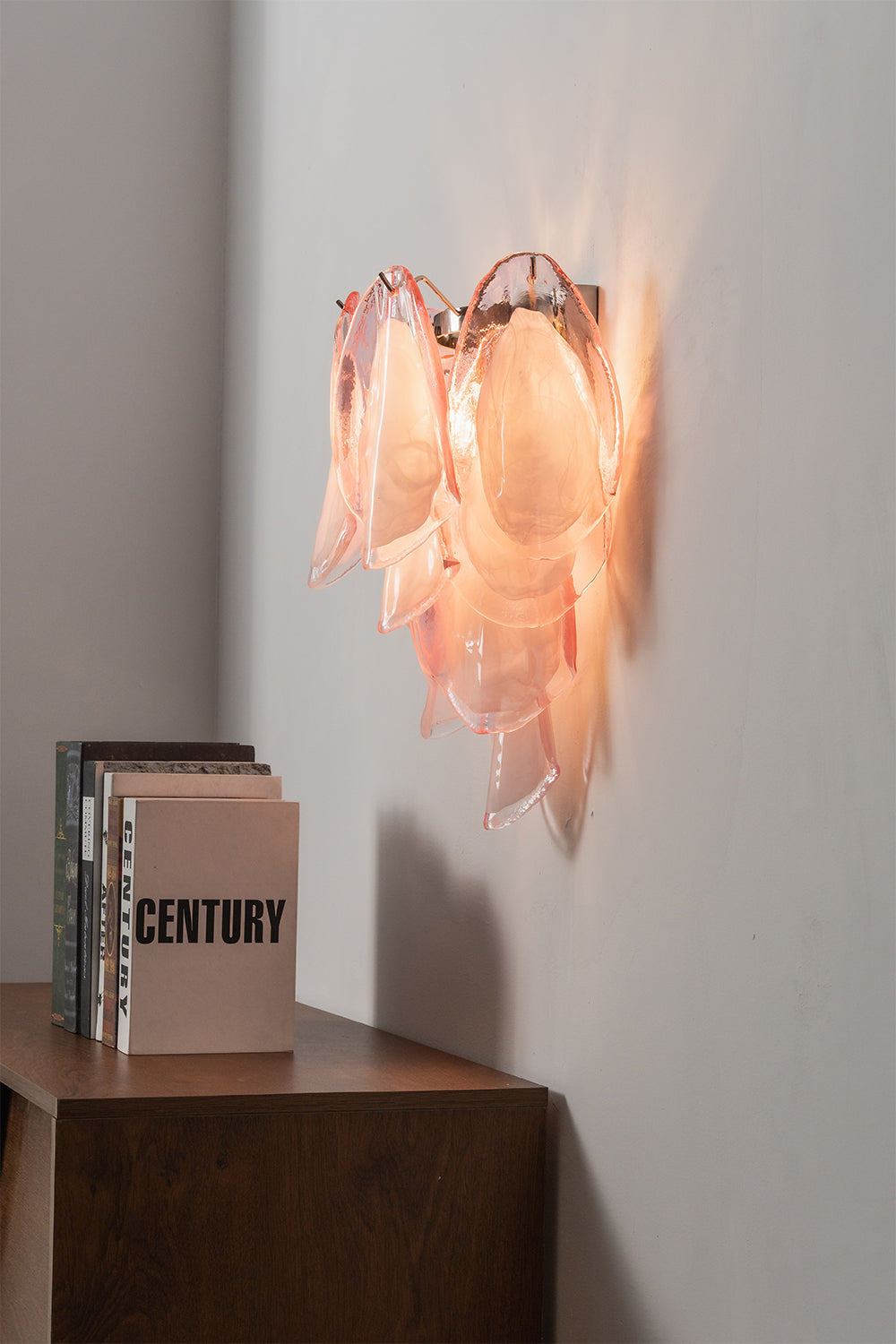 Elysian Bloom Glass Wall Lamp | Metal, Glass | Side angle view of the illuminated pink sconce radiating warm light over a cabinet | Samu Lamp