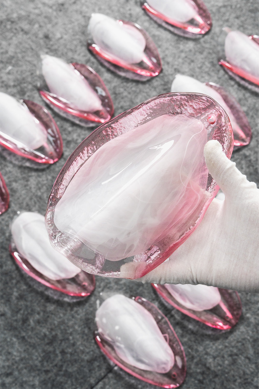 Elysian Bloom Rose Glass Chandelier | Metal, Glass | A gloved hand inspecting a single translucent pink glass petal surrounded by more glass components | Detail shot | Samu Lamp