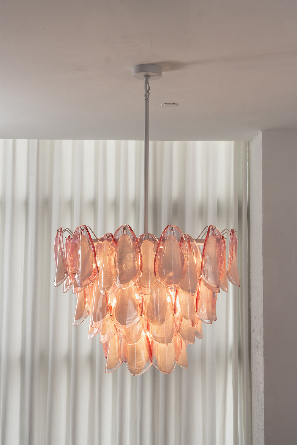 Elysian Bloom Rose Glass Chandelier | Metal, Glass | Fully lit chandelier casting a warm rosy glow in front of sheer white curtains | Samu Lamp