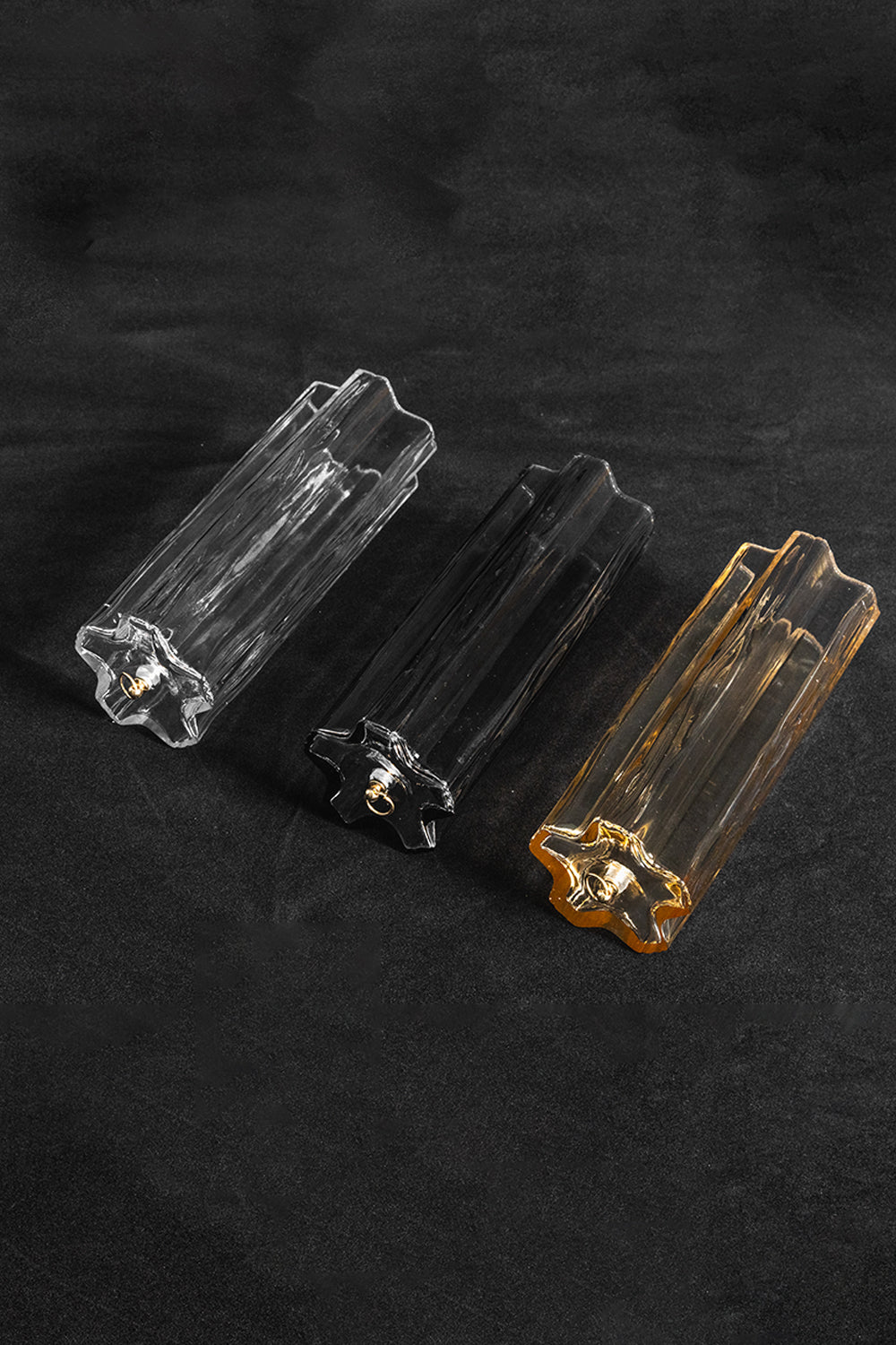 Elysian Tiered Fluted Ceiling Light | Glass, Metal | Close-up focus on three variant options of fluted glass prism rods (clear, smoky, and amber) resting on a black background | Detail shot | Samu Lamp