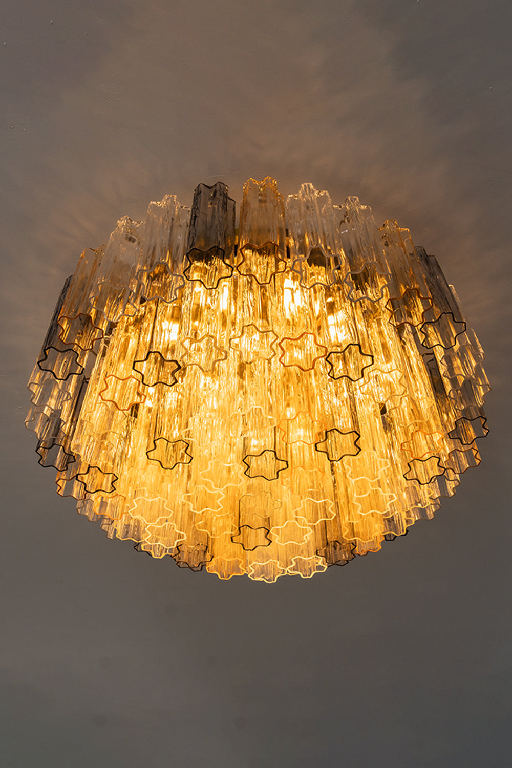Elysian Tiered Fluted Ceiling Light | Glass, Metal | Low-angle profile shot of the fully illuminated tiered flush mount fixture radiating a rich amber light halo against a dark ceiling | Samu Lamp