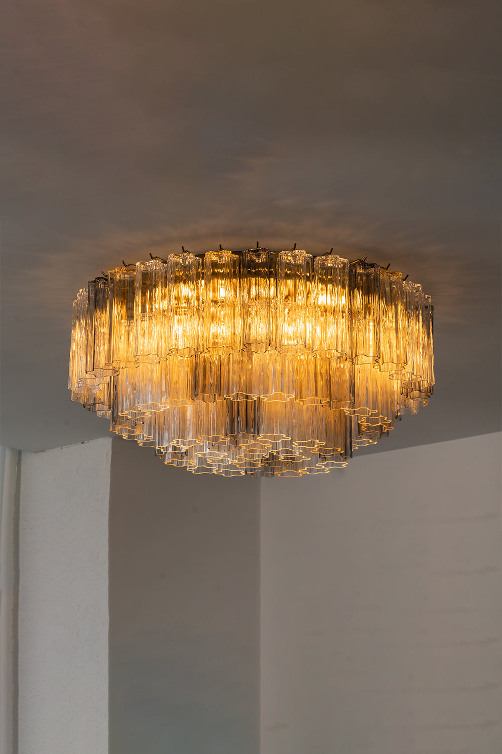 Elysian Tiered Fluted Ceiling Light | Glass, Metal | Side view of the illuminated multi-tiered glass ceiling light projecting a warm, inviting glow on a white studio ceiling | Samu Lamp