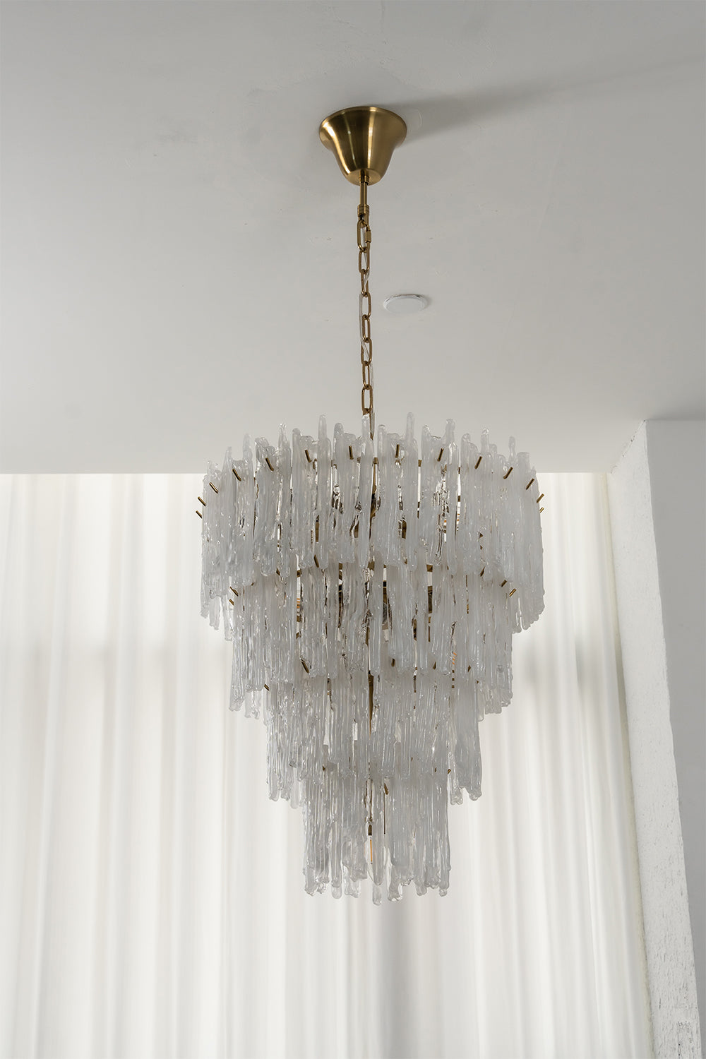 Ethereal Icicle Waterfall Chandelier | Glass, Metal | Unlit view of the tiered glass chandelier showcasing its crystalline elegance in front of sheer white blinds | Samu Lamp