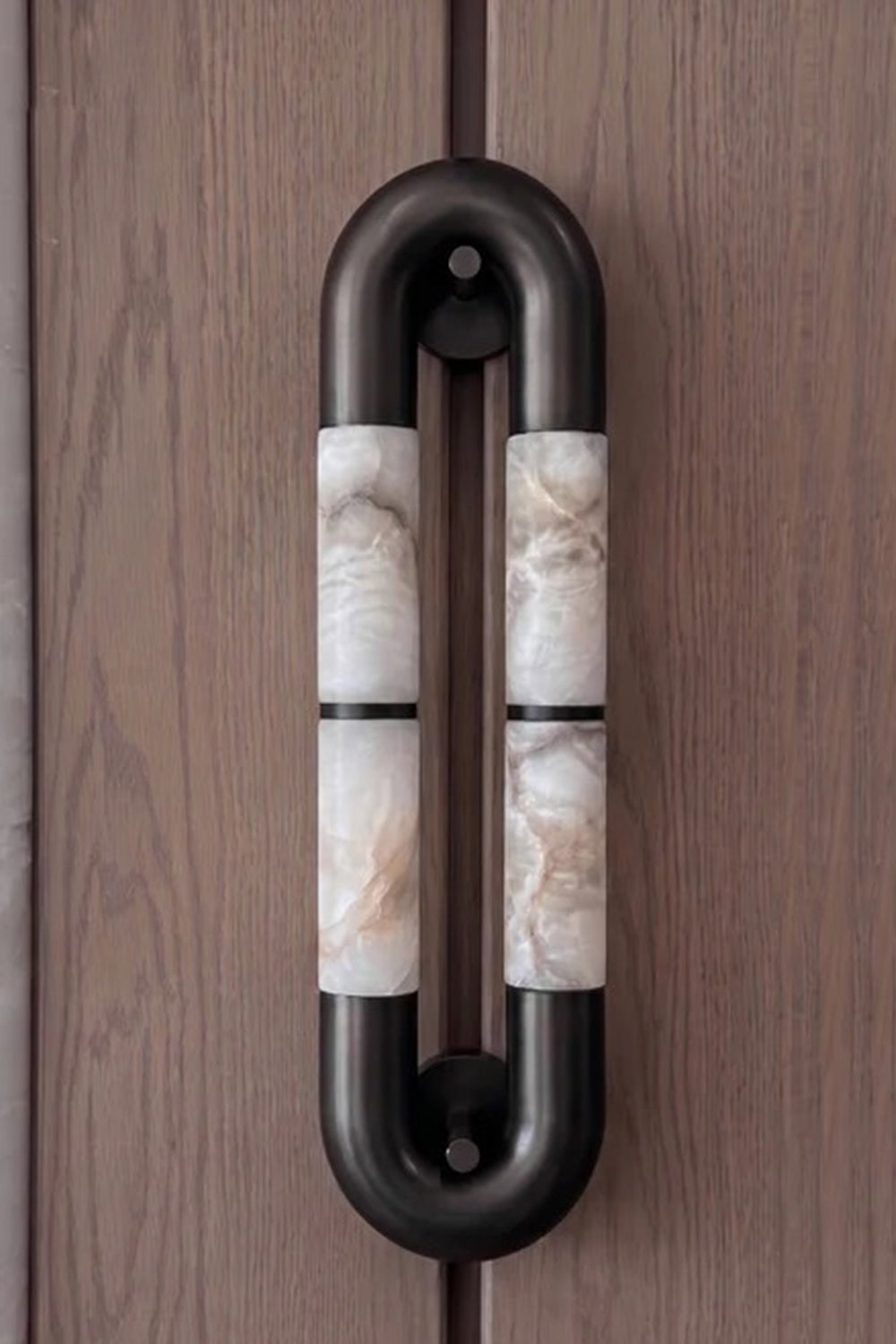 Evadne Alabaster Link Wall Sconce | Alabaster, Metal | Sconce unlit or in dim lighting mounted vertically on a dark wood-paneled wall, showing its architectural pill-shaped outline | Samu Lamp