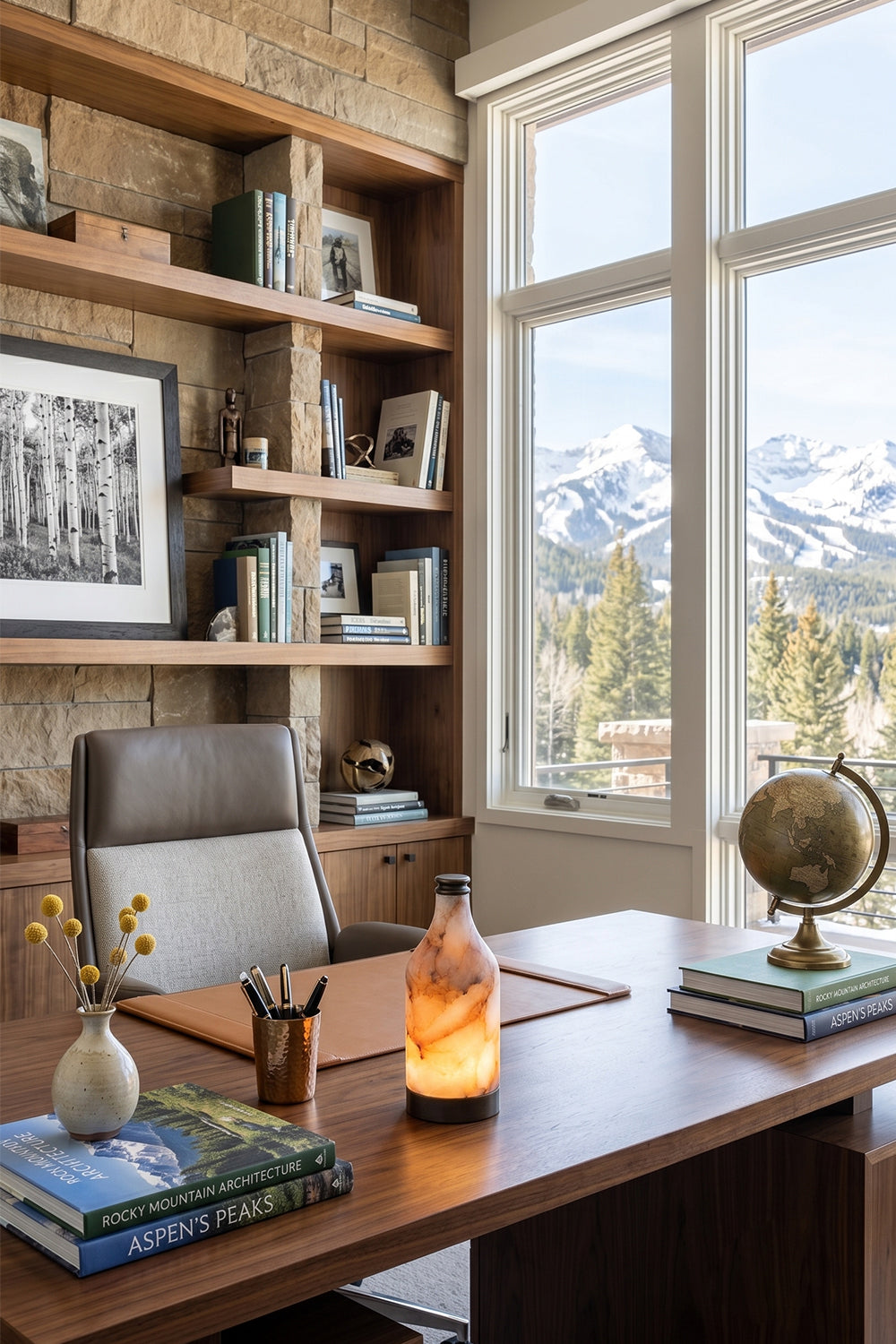 Evander Alabaster Bottle Table Lamp | Alabaster, Metal | Placed as cozy task lighting on a dark executive wooden desk in a rustic home library office with a scenic mountain view window | Samu Lamp