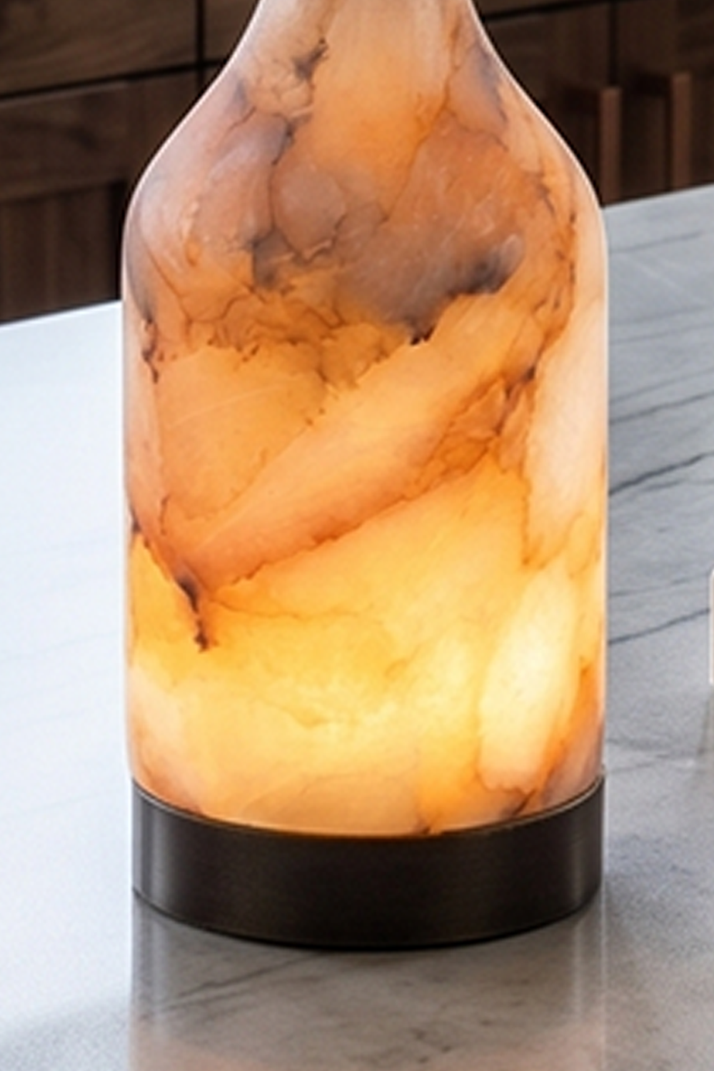 Evander Alabaster Bottle Table Lamp | Alabaster, Metal | Close-up shot highlighting the organic clouds, translucent stone body, and dark metal base on a polished kitchen countertop | Detail shot | Samu Lamp